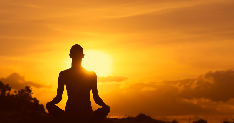 Woman meditating in a beautiful outdoor sunset setting.